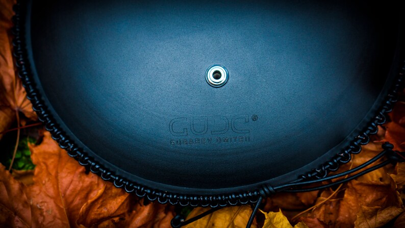 May include: A black leather drum with a black metal rim and a silver metal ring in the center. The drum has the word "GUDJ" and the text "FRABEN INGUIR" printed on it.