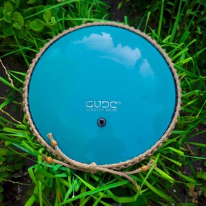 May include: A turquoise handpan with a rope handle and the text "GUD.C.O. GUAREV DRUM" on the surface.