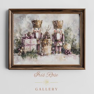 May include: A framed watercolor painting featuring two nutcrackers in gold and mauve uniforms, a gift box with a bow, a pinecone, and evergreen branches. The text Iris Rose GALLERY is printed below the frame in a light brown serif font.