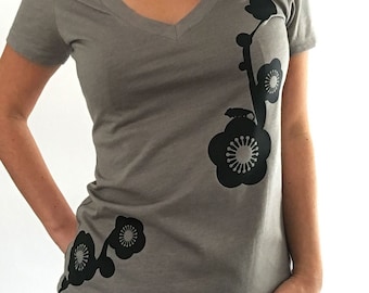 May include: A gray V-neck t-shirt with a black floral design. The design features stylized flowers and stems.