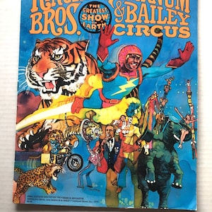 Peut inclure: Un programme souvenir du cirque Ringling Bros. and Barnum & Bailey de 1979 présentant une illustration vibrante d'un tigre, d'une figure de super-héros, d'un artiste sur une moto et d'un éléphant avec des acrobates sur un fond bleu vif.