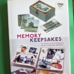 Puede incluir: Un libro titulado "Memory Keepsakes" con imágenes de una caja gris, postales y páginas de álbum de recortes. La portada presenta el título en rojo y morado, con el subtítulo "43 proyectos para crear y guardar recuerdos preciados."