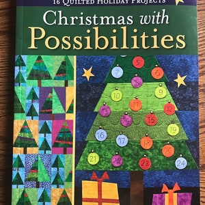 May include: A book titled "Christmas with Possibilities" featuring 16 quilted holiday projects. The cover displays a quilted Christmas tree with numbered ornaments and gift boxes. The book's cover has a green, blue, and gold color scheme.