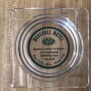 Peut inclure: Cendrier carré transparent avec un logo circulaire vert et blanc qui indique "MARSHALL MOTEL" et "AAA". Le texte comprend également "Courtesy Coffee In Rooms, Air Conditioned, Swimming Pool, Tile Bath, West Point, Miss., Phone 1125."