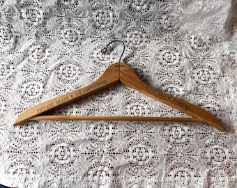 May include: A vintage wooden clothes hanger with the text "PRIVATE BEACH & AIR CONDITIONED" and "MIAMI BEACH, FLORIDA" printed on it. The hanger has a metal hook and is resting on a white lace surface.