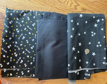 May include: Three pieces of black fabric with different patterns. One fabric has a white star pattern, one has a white ghost and yellow star pattern, and one is solid black.