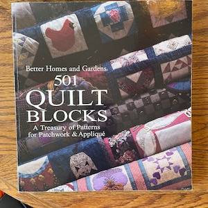 May include: A book titled "501 Quilt Blocks: A Treasury of Patterns for Patchwork & Appliqué" by Better Homes and Gardens. The cover features a variety of colourful quilt blocks.