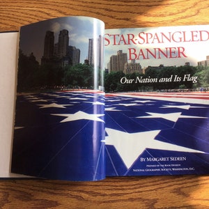 May include: A book titled "Star-Spangled Banner: Our Nation and Its Flag" by Margaret Sedeen. The cover features a close-up of a large American flag laid out on the ground with a city skyline in the background.