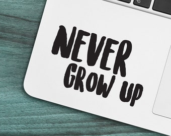 May include: A white laptop with a black "NEVER GROW UP" sticker on the lid. The laptop is on a teal wooden surface.