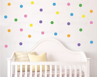 May include: A white crib with a white mattress and a white headboard. The wall behind the crib is white and has colorful polka dots in various colors, including pink, yellow, green, blue, and purple.
