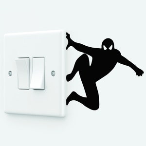 Könnte beinhalten: Ein weißer Lichtschalter mit zwei Kippschaltern, eine schwarze Silhouette einer Superheldenfigur klettert an der Wand hinter dem Schalter hoch.