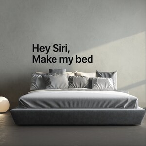 May include: A gray upholstered bed with a headboard and a gray bedspread. The text "Hey Siri, Make my bed" is written on the wall behind the bed.
