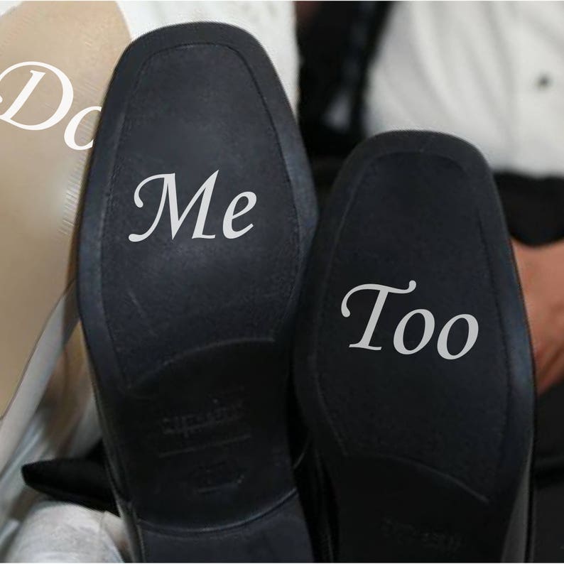 May include: A pair of black leather shoes with white text on the soles. One shoe says "Me" and the other says "Too".