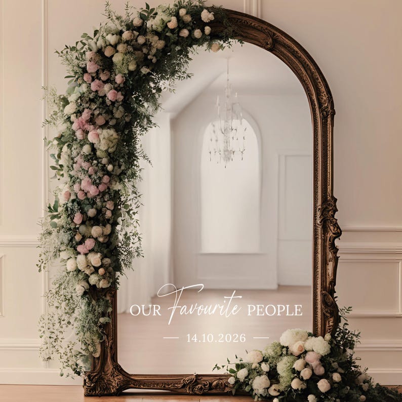 May include: A large, ornate, arched mirror with a dark wood frame. The mirror is decorated with a floral arrangement of white and pink roses, greenery, and the text "OUR Favourite PEOPLE" and the date "14.10.2026".
