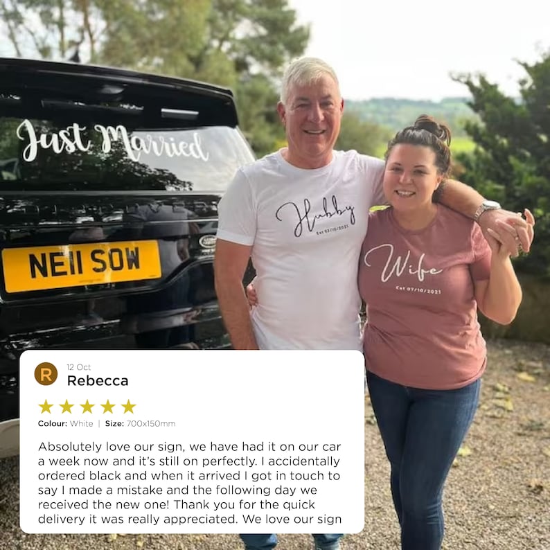 May include: A couple poses in front of a black car with a "Just Married" sign on the back window. The man is wearing a white t-shirt with the word "Hubby" written in cursive. The woman is wearing a pink t-shirt with the word "Wife" written in cursive. The car's license plate reads "NEII SOW".