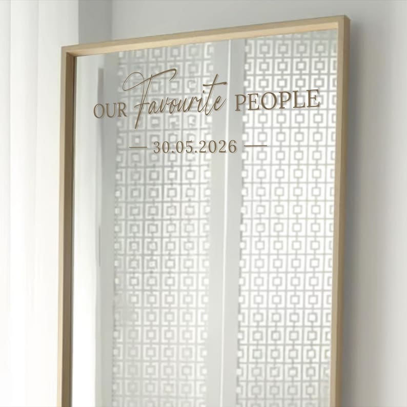 May include: A rectangular mirror with a gold frame. The mirror has the words "OUR Favourite PEOPLE" and the date "30.05.2026" in a decorative font. The background features a white geometric pattern.
