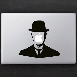 Puede incluir: Una silueta en blanco y negro de una persona con un sombrero de bombín con un logotipo de Apple que le cubre la cara. La silueta está en un portátil plateado.