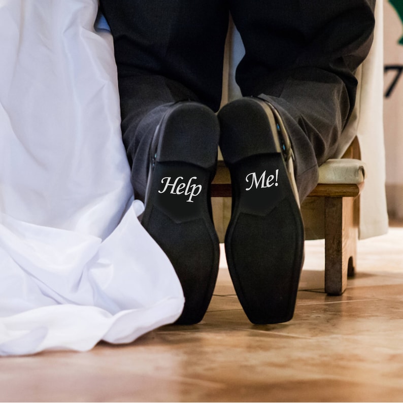 May include: A pair of black dress shoes with the words "Help" and "Me!" written on the soles.