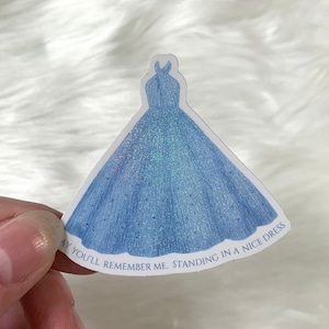 May include: A blue glitter sticker of a ball gown with the text "May you'll remember me, standing in a nice dress".