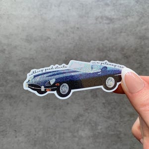 May include: A sticker depicting a classic blue sports car with the text "nothing good starts in a getaway car." The car has silver wheels and a glittery finish, creating a shimmering effect.