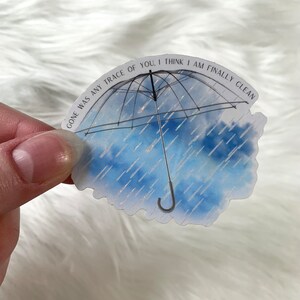 May include: A blue and white watercolour sticker with a black umbrella and the text "Gone was any trace of you, I think I am finally clean".
