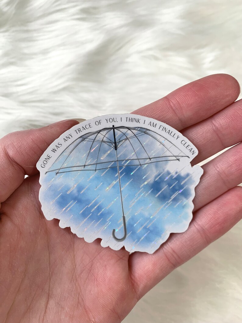 May include: A white sticker with a black outline of an umbrella with a blue and white watercolour background. The text on the sticker reads "Gone was any trace of you. I think I am finally clean."