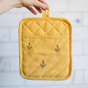 May include: A yellow quilted hot pad with a pocket and embroidered floral designs.