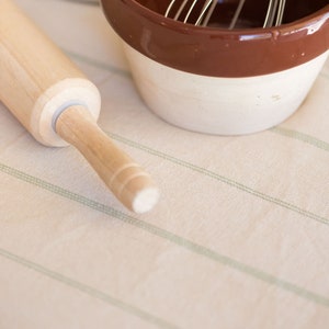 May include: A wooden rolling pin and a brown and white ceramic bowl with a wire whisk inside, on a striped tablecloth.