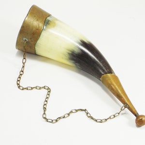 May include: A brown and white horn drinking cup with a brass rim and a brass chain attached to a brass ball at the end.
