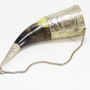 May include: A silver and brown drinking horn with a chain attached. The horn is decorated with a silver band and intricate designs.