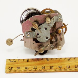 May include: Close-up of a vintage clockwork mechanism with a spring, gears, and a winding key. The mechanism is about 3.8 cm wide and is made of metal.