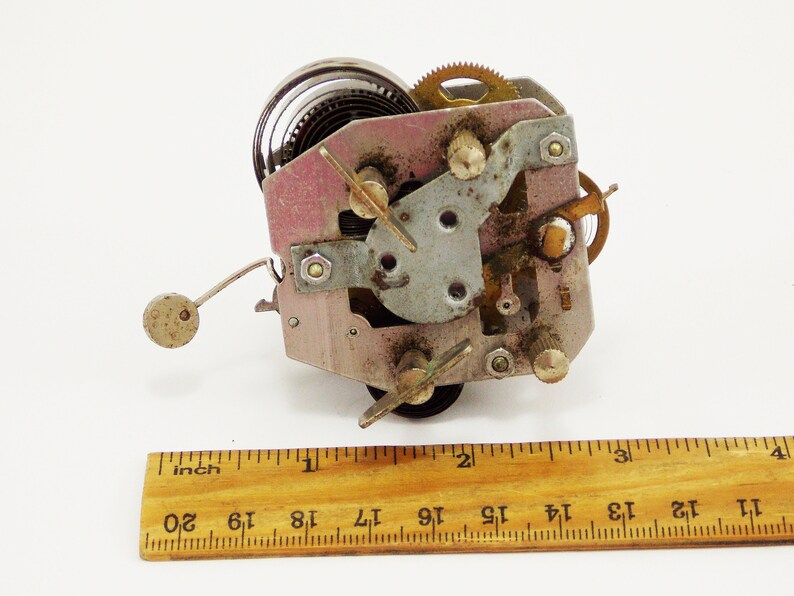 May include: Close-up of a vintage clockwork mechanism with a spring, gears, and a winding key. The mechanism is about 3.8 cm wide and is made of metal.