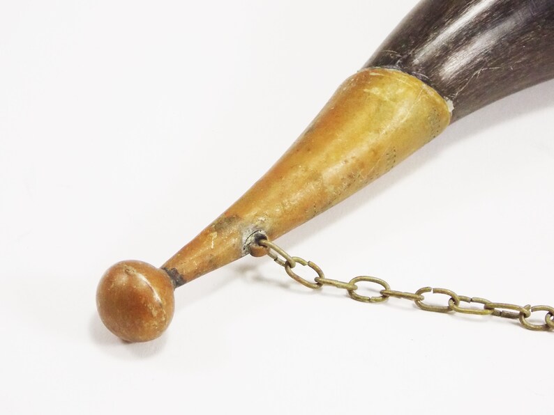 May include: A brown and black horn with a brass tip and a brass chain attached. The horn is about 12 inches long.