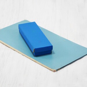 Pode incluir: Uma caixa retangular azul est&aacute; em cima de um peda&ccedil;o de papel&atilde;o retangular azul claro.