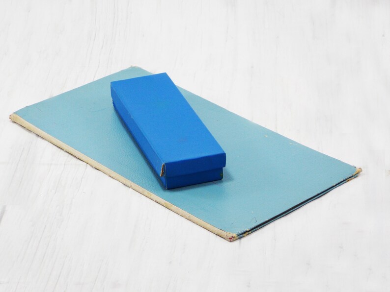 Pode incluir: Uma caixa retangular azul est&aacute; em cima de um peda&ccedil;o de papel&atilde;o retangular azul claro.