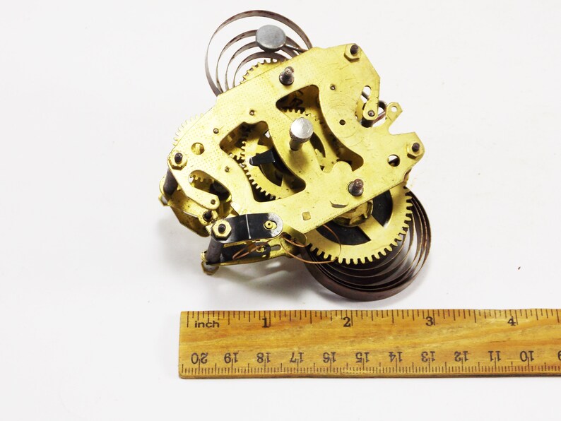 May include: A gold-coloured clock mechanism with a spring and gears. The mechanism is approximately 5 cm wide and 5 cm tall.