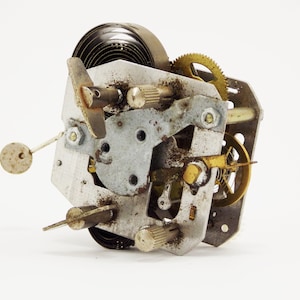 May include: Close-up of a vintage clock mechanism with a metal spring, gears, and a brass winding key. The mechanism is rusty and shows signs of wear and tear.
