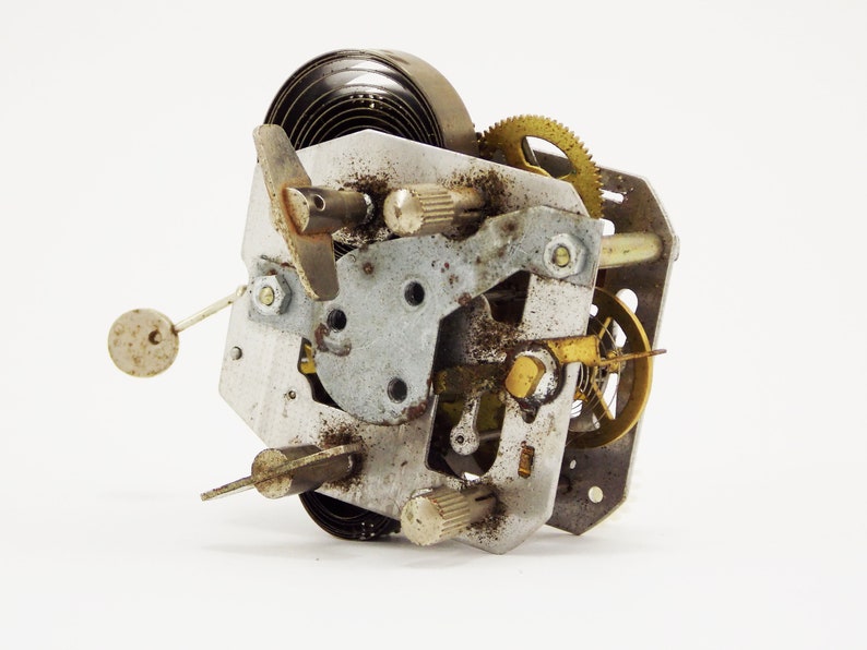 May include: Close-up of a vintage clock mechanism with a metal spring, gears, and a brass winding key. The mechanism is rusty and shows signs of wear and tear.