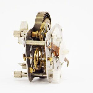May include: Close-up of a disassembled clock mechanism with gears, springs, and metal parts.