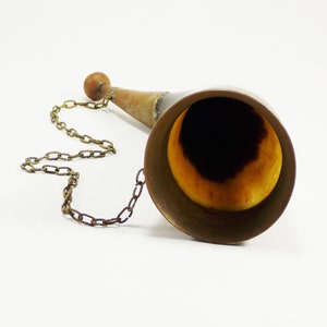 May include: A brass horn with a wooden handle and a chain attached. The horn is polished and has a golden hue.