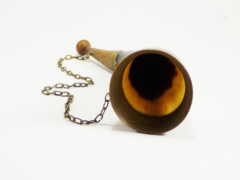 May include: A brass horn with a wooden handle and a chain attached. The horn is polished and has a golden hue.