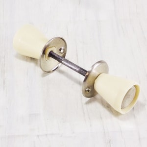 May include: A pair of off-white door knobs with a silver metal base and a metal rod connecting them.