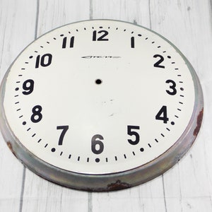 May include: A white clock face with black numbers and hands. The clock face is surrounded by a silver metal rim. The clock face has the word "СССР" printed on it.