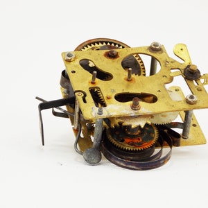 May include: Close-up of a vintage clock mechanism with brass gears and a metal spring. The mechanism is disassembled and shows signs of wear and age.