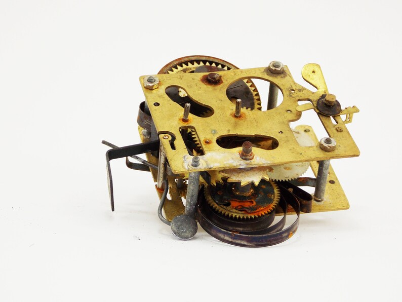 May include: Close-up of a vintage clock mechanism with brass gears and a metal spring. The mechanism is disassembled and shows signs of wear and age.