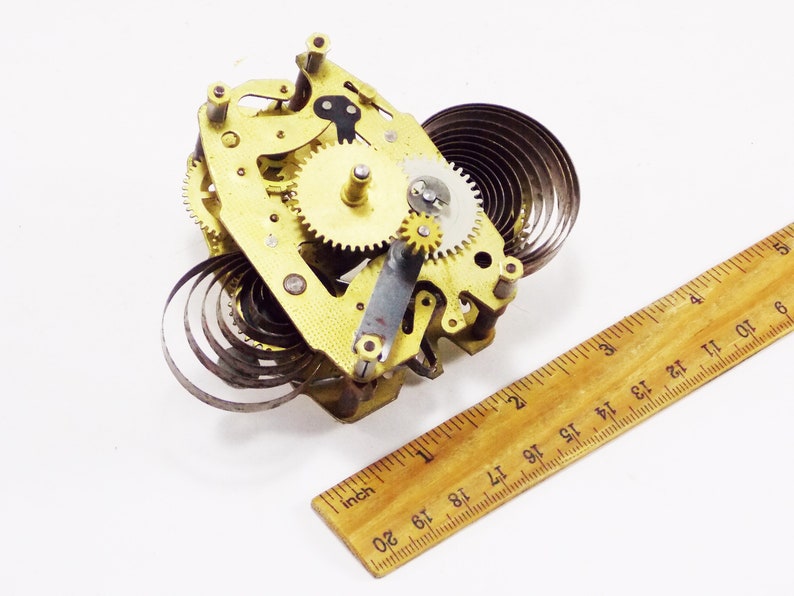 May include: Close-up of a gold-coloured clockwork mechanism with a coiled spring. The mechanism is about 5 cm wide and 5 cm tall.