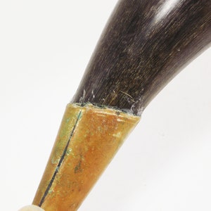 May include: A dark brown powder horn with a brass tip and a chain attached. The horn is made of natural material and has a rustic look.