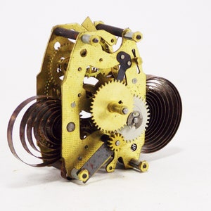 May include: Close-up of a gold-coloured clockwork mechanism with a coiled spring and multiple gears. The mechanism is isolated on a white background.