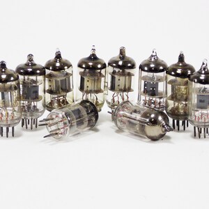 May include: A group of eight vintage vacuum tubes, all clear glass with a silver metallic top, arranged on a white surface.