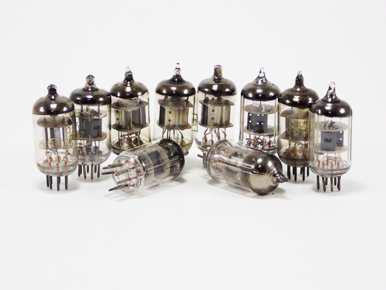 May include: A group of eight vintage vacuum tubes, all clear glass with a silver metallic top, arranged on a white surface.